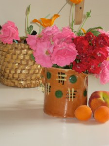 Photo shows vase of roses, apricots, basket.